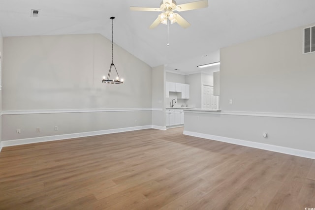 unfurnished living room with ceiling fan with notable chandelier, vaulted ceiling, light wood-type flooring, and baseboards