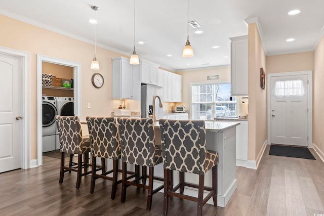 kitchen featuring ornamental molding, a breakfast bar, dark wood-type flooring, and washing machine and clothes dryer