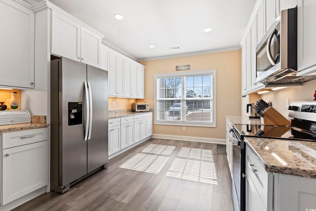 kitchen with white cabinets, ornamental molding, stainless steel appliances, and wood finished floors