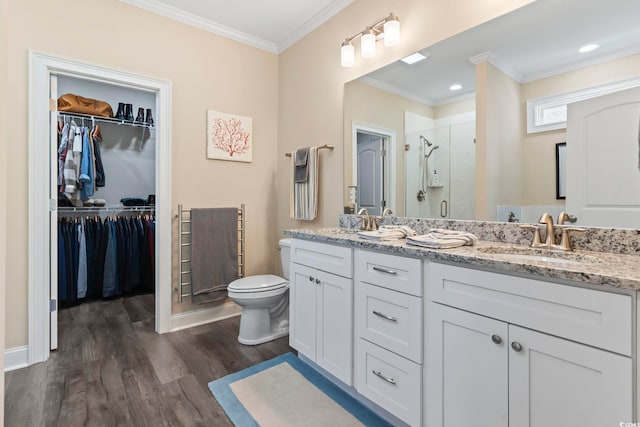 full bathroom featuring a walk in closet, ornamental molding, a stall shower, a sink, and wood finished floors