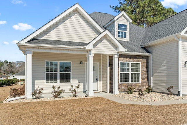 view of front of property with stone siding, a shingled roof, a front lawn, and covered porch