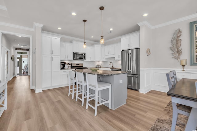 kitchen featuring a kitchen island, light wood-style flooring, a kitchen breakfast bar, stainless steel appliances, and white cabinetry