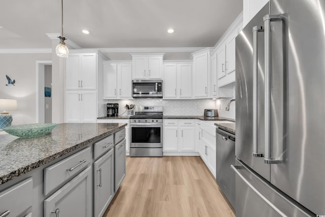 kitchen with tasteful backsplash, decorative light fixtures, ornamental molding, light wood-style floors, and stainless steel appliances