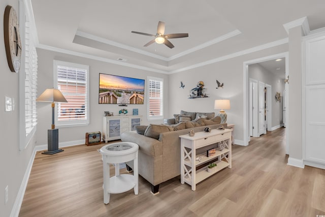 living area with baseboards, light wood-type flooring, a tray ceiling, ornamental molding, and a ceiling fan