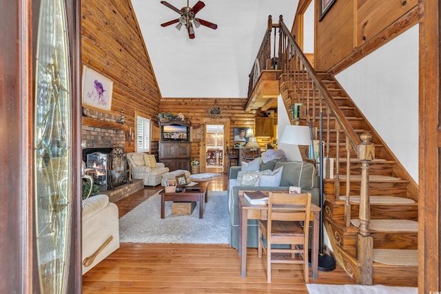 living area with rustic walls, a brick fireplace, stairs, and wood finished floors