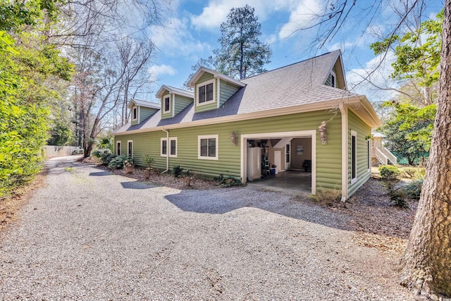 view of side of home featuring gravel driveway, an attached garage, and roof with shingles