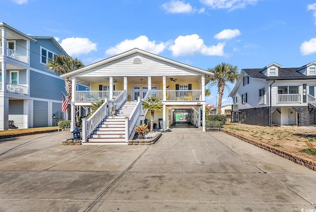 raised beach house featuring a ceiling fan, concrete driveway, stairway, a porch, and a carport