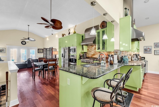 kitchen with stainless steel appliances, green cabinetry, a sink, and wall chimney exhaust hood