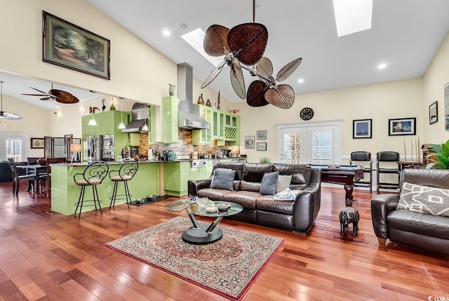 living room with a skylight, a ceiling fan, french doors, light wood-style floors, and high vaulted ceiling