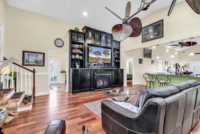 living area with high vaulted ceiling, light wood-style floors, stairway, and a ceiling fan