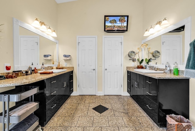 bathroom featuring a sink, two vanities, a towering ceiling, and baseboards