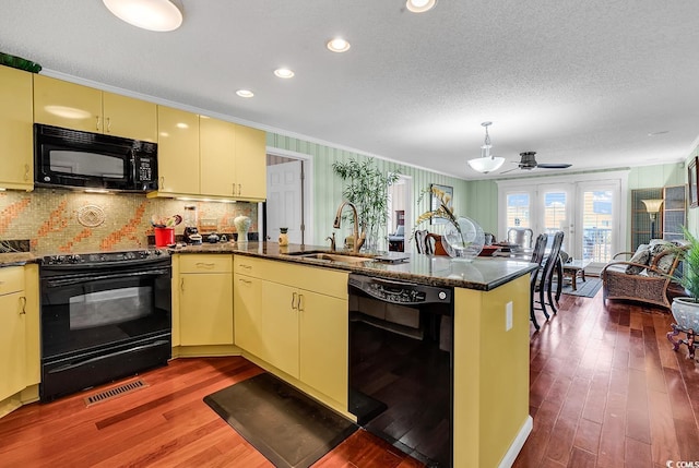 kitchen with cream cabinets, a peninsula, wood finished floors, a sink, and black appliances