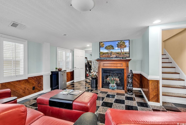 living room featuring a textured ceiling, a wainscoted wall, wood walls, visible vents, and stairway