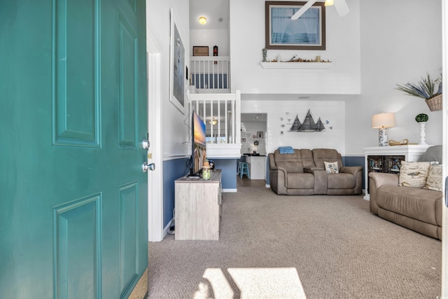 carpeted living room with ceiling fan and a towering ceiling