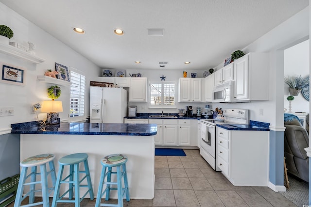 kitchen with white appliances, light tile patterned floors, a breakfast bar area, a peninsula, and white cabinetry