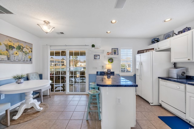 kitchen with dark countertops, white appliances, light tile patterned flooring, and visible vents