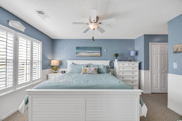 bedroom featuring visible vents, a wainscoted wall, ceiling fan, carpet, and a textured ceiling