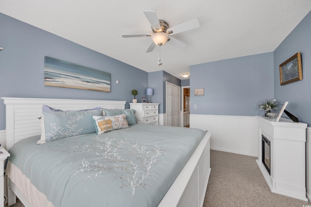 carpeted bedroom with a ceiling fan, a glass covered fireplace, and a closet