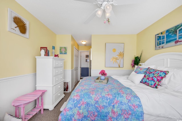 carpeted bedroom with wainscoting and ceiling fan