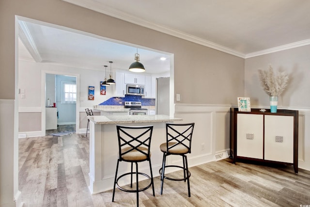kitchen with light wood finished floors, appliances with stainless steel finishes, ornamental molding, white cabinetry, and a kitchen bar