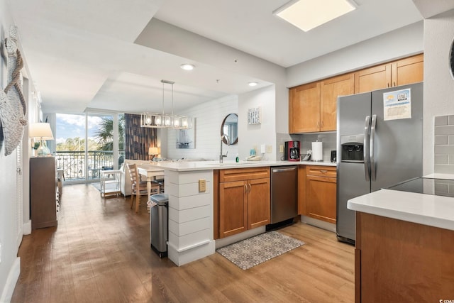 kitchen featuring a peninsula, light wood-style floors, stainless steel appliances, and decorative backsplash