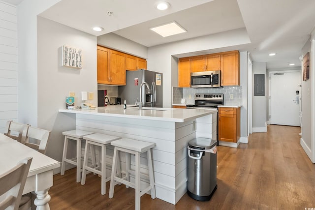 kitchen with stainless steel appliances, tasteful backsplash, light wood-style floors, electric panel, and a peninsula