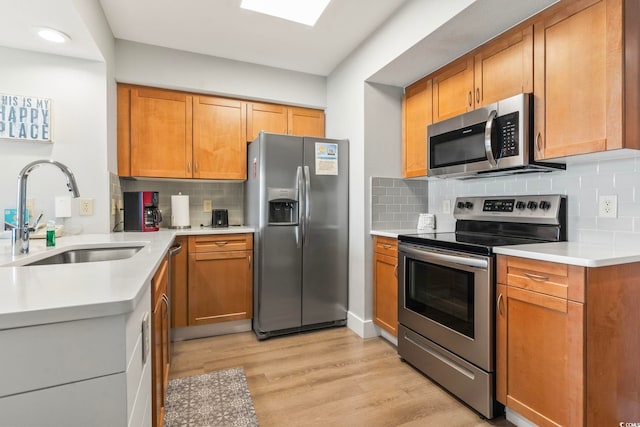 kitchen with decorative backsplash, appliances with stainless steel finishes, light countertops, light wood-style floors, and a sink