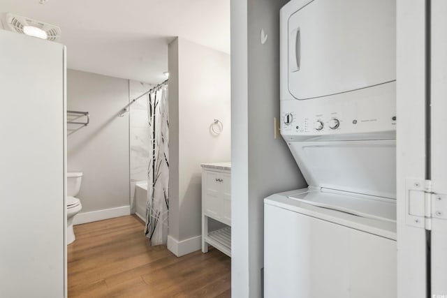 washroom featuring stacked washer and dryer, baseboards, laundry area, and wood finished floors