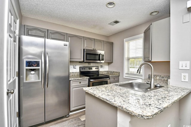 kitchen with gray cabinetry, a peninsula, a sink, visible vents, and appliances with stainless steel finishes