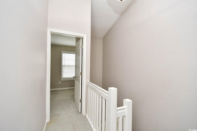 hall featuring baseboards, light carpet, and an upstairs landing