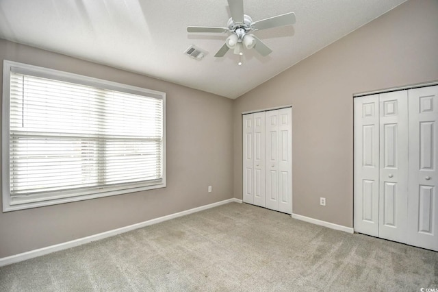 unfurnished bedroom with carpet flooring, visible vents, baseboards, vaulted ceiling, and two closets