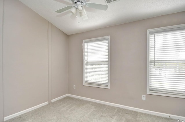 spare room featuring a textured ceiling, light colored carpet, visible vents, baseboards, and a ceiling fan