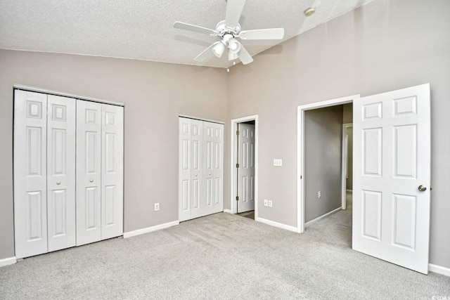 unfurnished bedroom featuring carpet floors, multiple closets, lofted ceiling, a textured ceiling, and baseboards