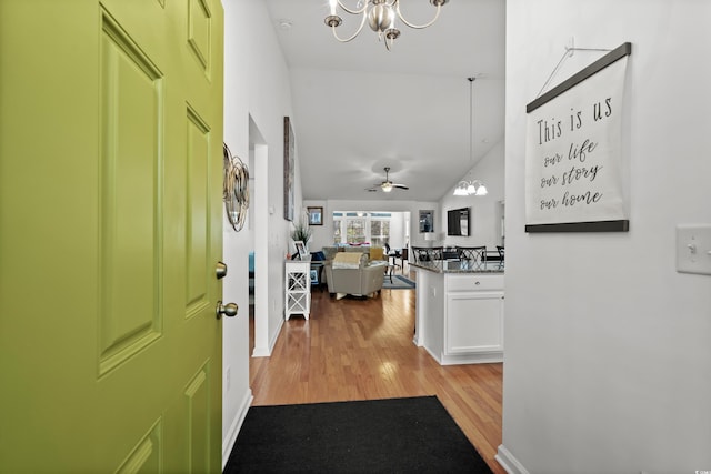 entrance foyer featuring lofted ceiling, light wood finished floors, ceiling fan with notable chandelier, and baseboards