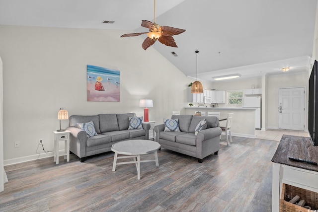 living area with visible vents, ceiling fan, high vaulted ceiling, light wood-type flooring, and baseboards