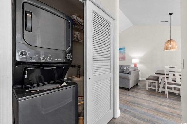 washroom with visible vents, stacked washing maching and dryer, wood finished floors, laundry area, and baseboards