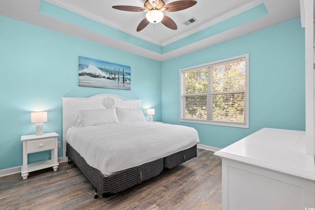 bedroom with a tray ceiling, visible vents, dark wood-type flooring, ornamental molding, and baseboards