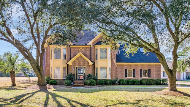 view of front facade with a shingled roof, brick siding, and a front lawn