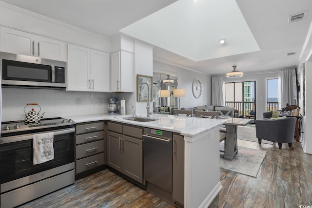 kitchen featuring visible vents, appliances with stainless steel finishes, open floor plan, a peninsula, and a sink