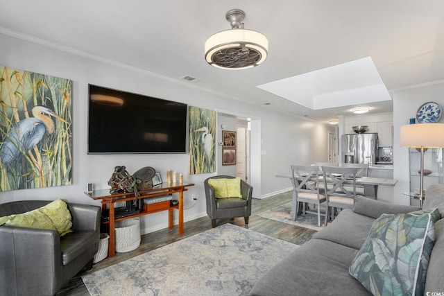 living area with a skylight, wood finished floors, visible vents, baseboards, and crown molding