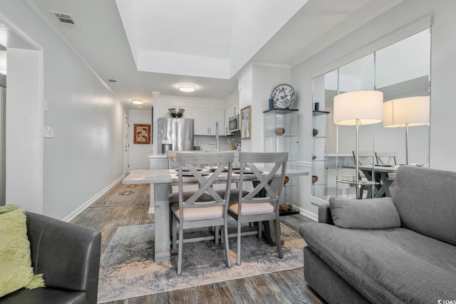 dining room with crown molding, a raised ceiling, visible vents, wood finished floors, and baseboards