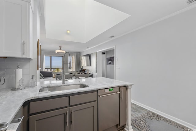 kitchen featuring gray cabinetry, a peninsula, a sink, backsplash, and light stone countertops