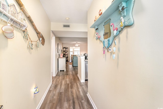 hallway featuring baseboards, a textured ceiling, visible vents, and wood finished floors