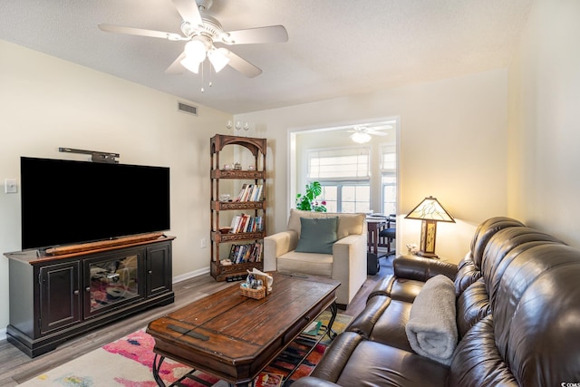 living room with light wood-type flooring, a textured ceiling, visible vents, and a ceiling fan