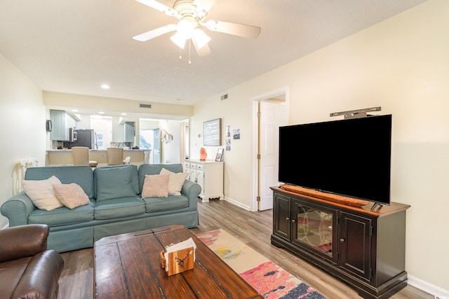 living room featuring baseboards, a ceiling fan, visible vents, and light wood-style floors