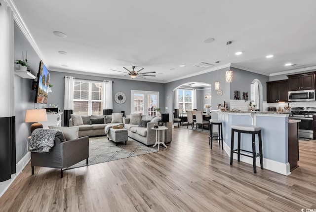 living room featuring arched walkways, a ceiling fan, light wood-style flooring, crown molding, and recessed lighting