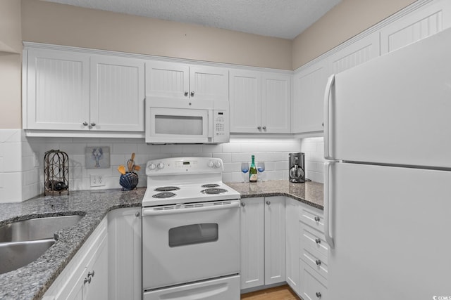 kitchen with a textured ceiling, stone countertops, white appliances, white cabinetry, and backsplash