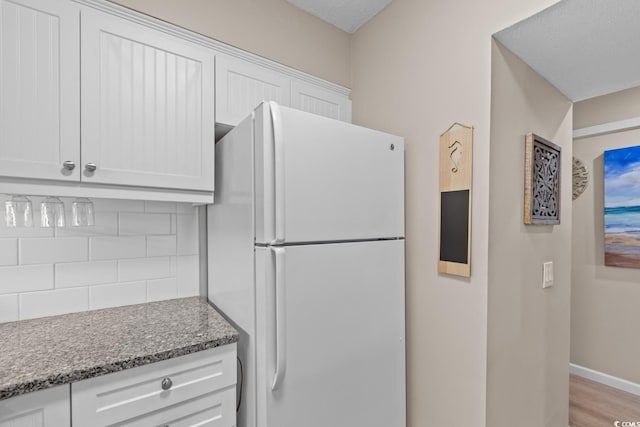 kitchen featuring tasteful backsplash, dark stone countertops, freestanding refrigerator, and white cabinets