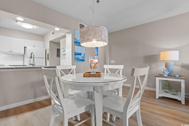 dining area with a textured ceiling, light wood-type flooring, visible vents, and baseboards