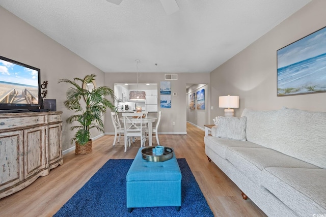 living room with a textured ceiling, light wood finished floors, visible vents, and baseboards